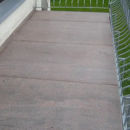 Balkon mit Metallgeländer nach der Sanierung: großformatige rotbraun-graue Natursteinplatten – InnoStone Treppensanierung