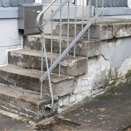 Stark geschädigte Betontreppe vor der Sanierung: abplatzender Putz, ausgebrochene Wange
