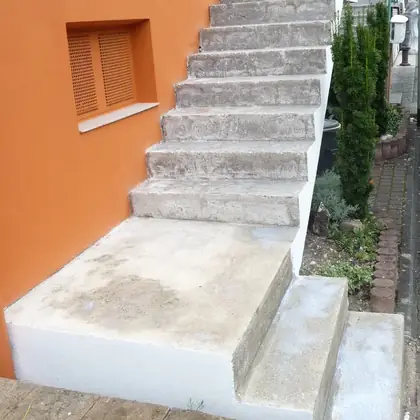 Außentreppe an oranger Fassade vor der Sanierung: ausgetretener Beton mit breitem Antrittspodest