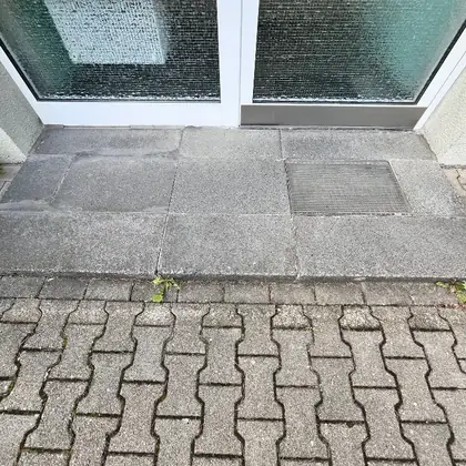 Eingangspodest vor der Glastür vor der Sanierung: alte graue Platten, unterschiedliche Formate